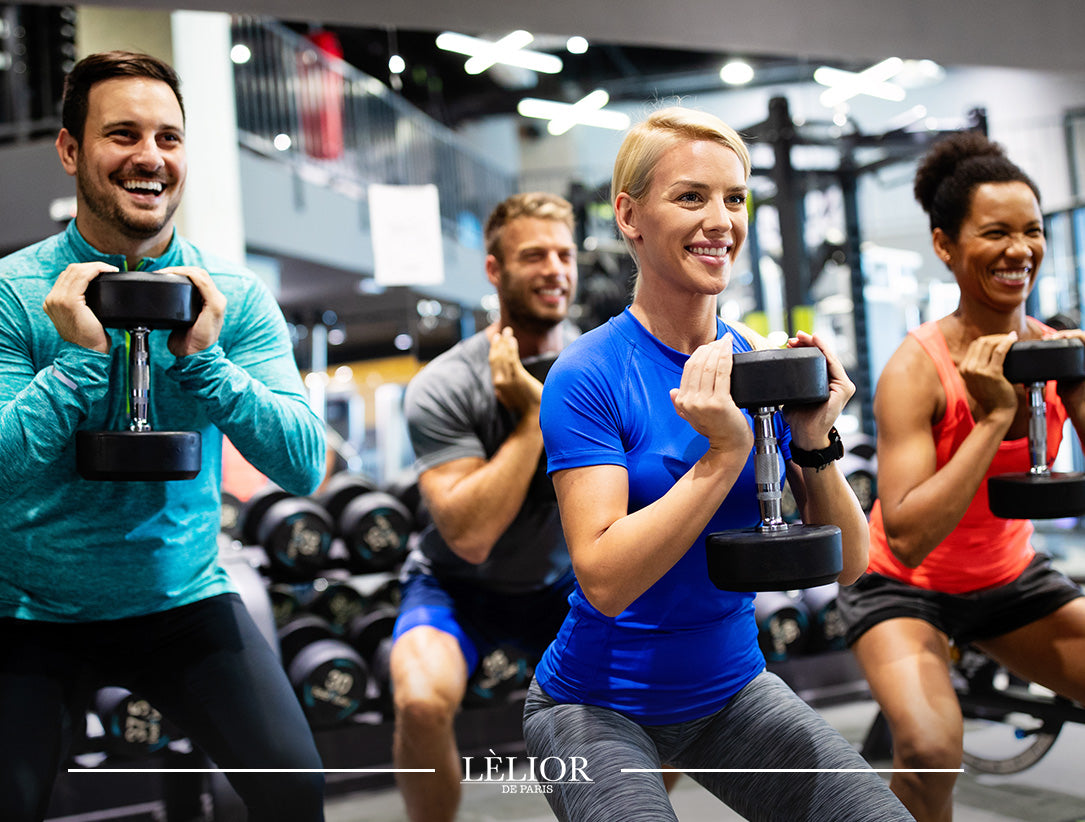 Two men and two women holding dumbells, squatting and working out in the gym