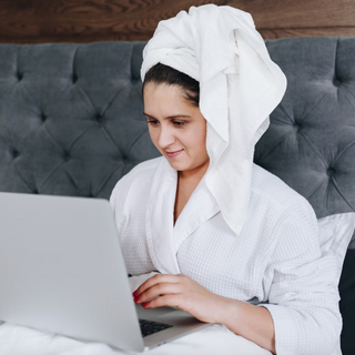 Woman in a bathrobe works on her laptop from her hotel bed