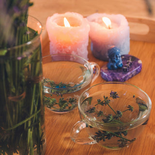 A pair of lit candles and teacups sit on a wooden tray